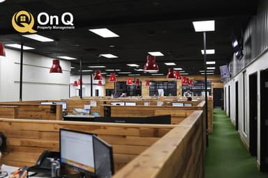 The open bullpen at the On Q Property Management office in Gilbert, with wood-paneled desk pods, red pendant lights, and the On Q logo in the upper left corner